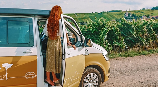 a girl with read hair standing on the threshold of a VW campervan