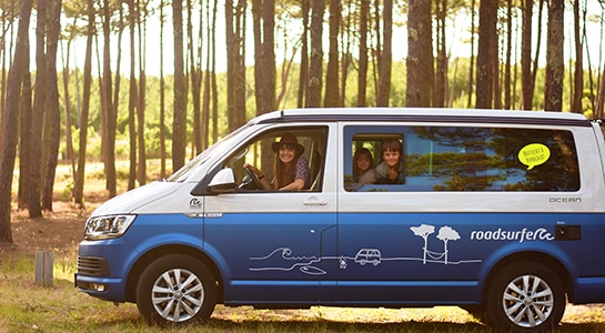 A family sitting in a blue VW campervan from roadsurfer