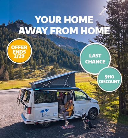 Girl sits in a campervan with a pop up roof next to her dog in the mountains