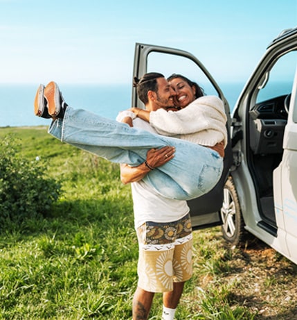 Man carrying a woman in his arms in front of a campervan.