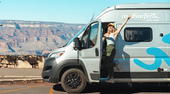 Woman standing in the doorway of a boxvan, leaning out and waving her hand up in the air.