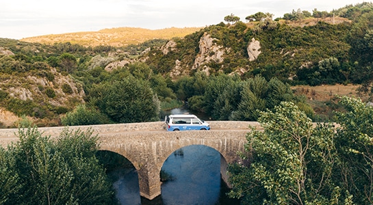 blue campervan driving on a bridge throughout