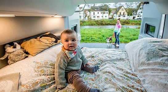 Baby seating on the bed of a VW Grand California camper with open doors