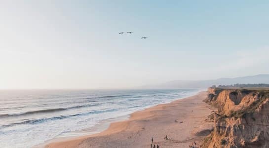 View from a coastal bluff overlooking Half Moon Bay’s sandy shoreline, ocean waves, and warm evening light along the cliffs.