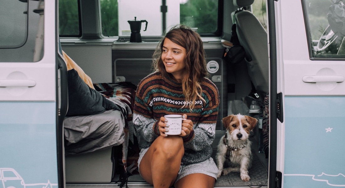 Woman sitting in VW campervan with her dog drinking a cup of tea