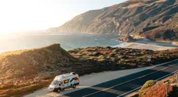 Grey RV driving alongside the american coast during sunset.