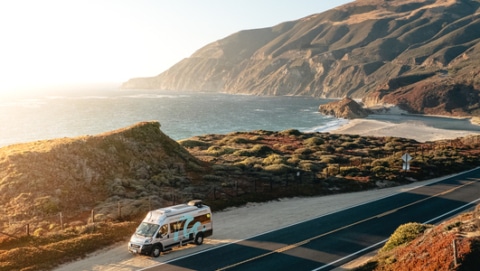 Grey RV driving alongside the american coast during sunset.