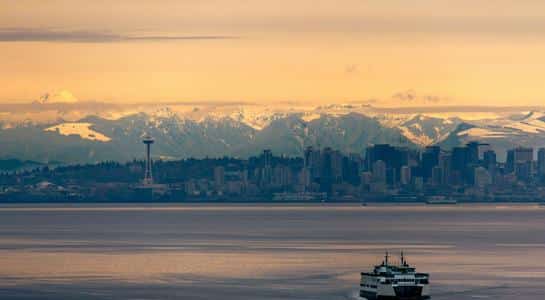 Seattle skyline and Space Needle with Olympic Mountains in the background and a ferry on Puget Sound.
