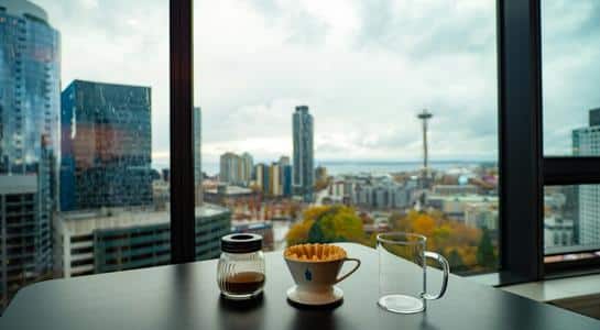 Seattle skyline view from a window with coffee brewing setup in the foreground.