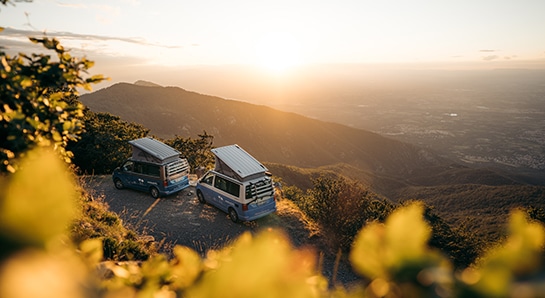 two VW California camper standing on a hill with open roof looking into the sunset