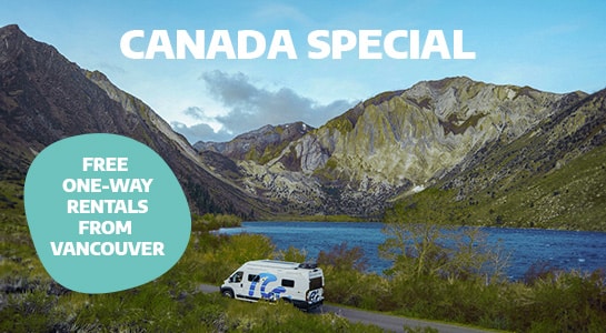 A camper van driving through canadian landscape next to a lake and mountains