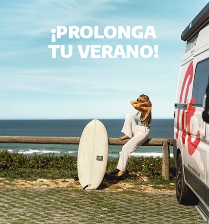 Girl sitting next to her surfboard near to a parked campervan at the beach.