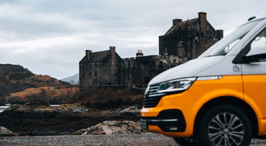 Yellow VW camper from roadsurfer standing in front of a castle in Scotland