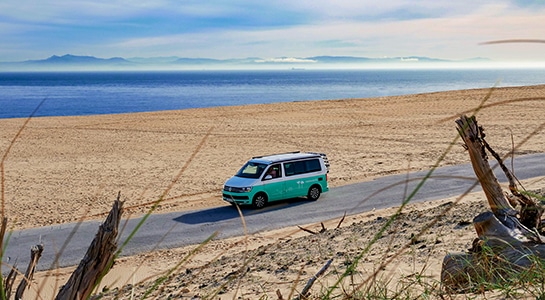 Turquoise VW campervan driving on a road along a beach