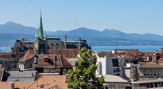 Aerial shot of historical buildings in Lausanne with Lake Geneva and the mountains in the background.