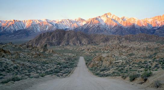 Dirt road winding through the Alabama Hills at sunrise, with Mount Whitney and the snow-capped Sierra Nevada in the background—an iconic stop on a California road trip
