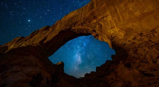 Milky Way visible through a sandstone arch in Arches National Park, a stunning night photography spot during a Colorado to California road trip.