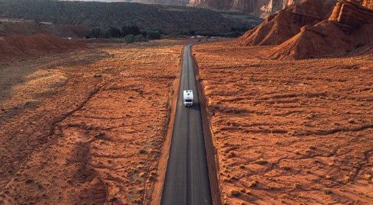 roadsurfer RV driving along an empty desert highway surrounded by red rock cliffs on an Arizona road trip itinerary