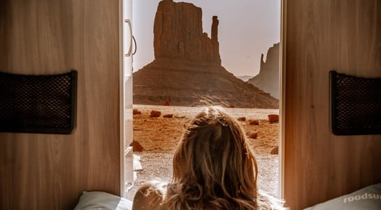 Woman lying inside an RV looking out at Monument Valley during an Arizona road trip