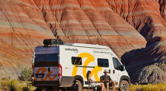 Couple relaxing beside their RV in Williams, Arizona, surrounded by colorful red hills on an Arizona road trip