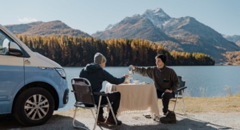 two men sitting in front of their van, having coffee at a table