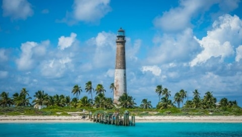 Tropical beach scene with turquoise water, palm trees, and a weathered lighthouse resembling Bahia Honda State Park in the Florida Keys