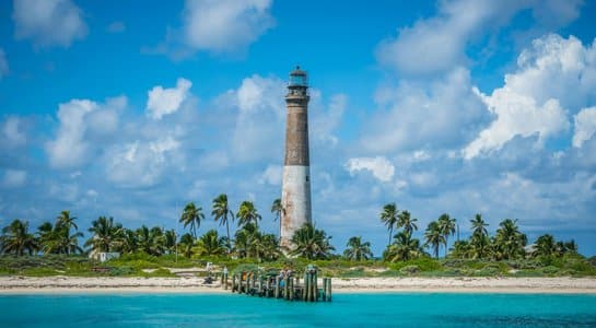 Tropical beach scene with turquoise water, palm trees, and a weathered lighthouse resembling Bahia Honda State Park in the Florida Keys