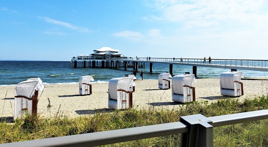 Beach huts on a beach at the Baltic Sea with pier visible in the background.