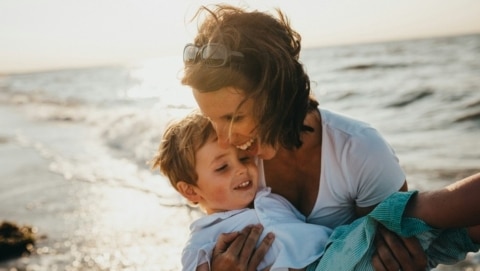 A mother and child smiling together at the beach during sunset, showing one of the fun things to do in California with kids on a family trip.