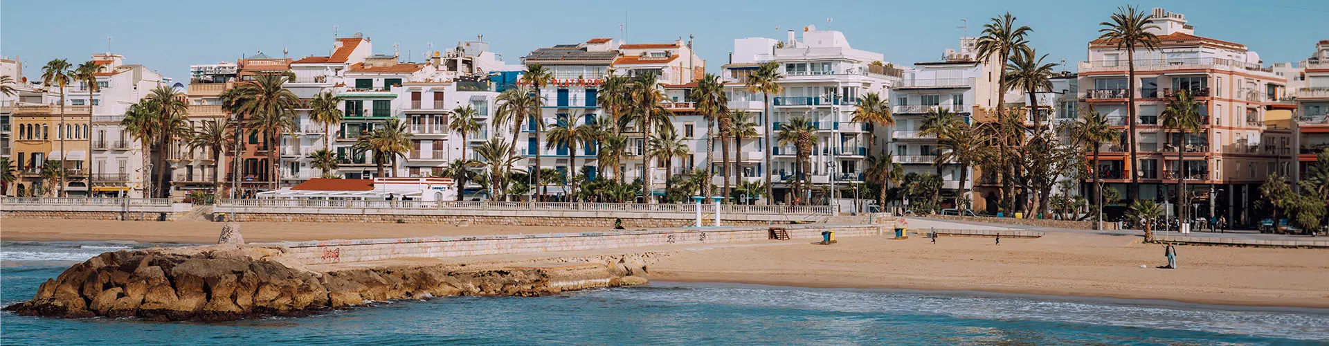 Sitges beach on the Costa Dorada, Catalonia, with colourful buildings in the background and a blue sky.