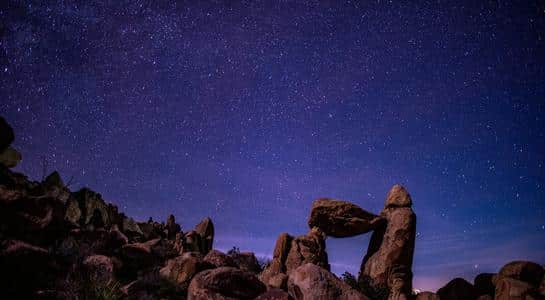 Star-filled night sky above Balanced Rock in Big Bend National Park, Texas, with desert rocks in silhouette.