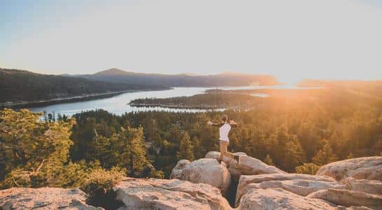 Hiker at a rocky overlook watching sunrise above Big Bear Lake, part of a weekend getaway from Los Angeles