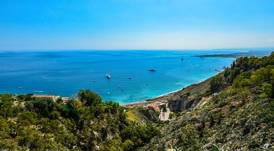 Bird view over turquoise sea in Sicily, showing not only the sea but also green hills during a sunny day.