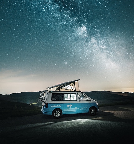 Blue campervan with opened pop up roof parked beneath starry sky