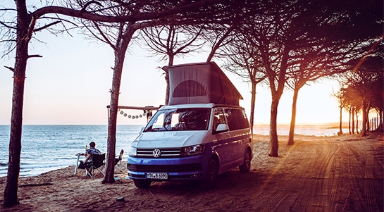 blue campervan with pop up roof at the beach under trees