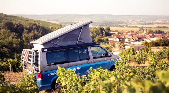 Blue roadsurfer campervan parked on a hill in a vineyard