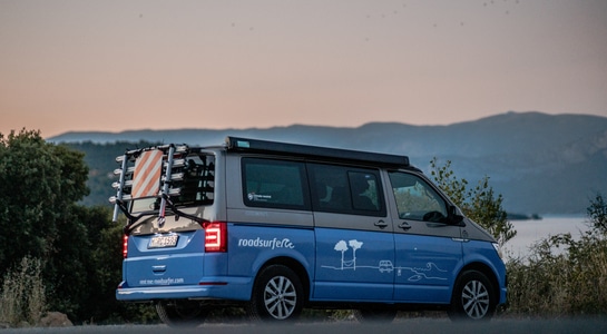 Blue roadsurfer campervan standing near to the sea during the sunset