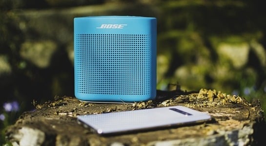 Blue bluetooth speaker and phone laying on a tree stump.