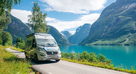 Boxvan driving alondside a fjord in Norway on a sunny day.