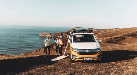 Three boys with their surfboards and a campervan at the atlantic coast