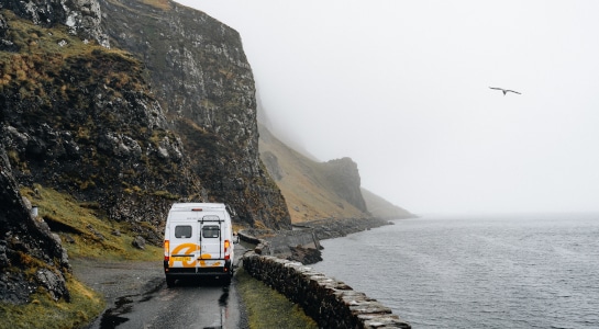 Campervan driving along a cliff road on a foggy day