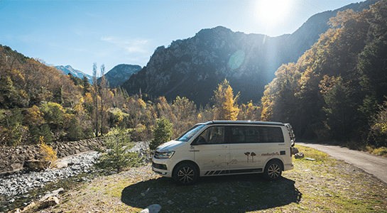 Camper parked on the slope of a river in a mountain landscape of Andorra.