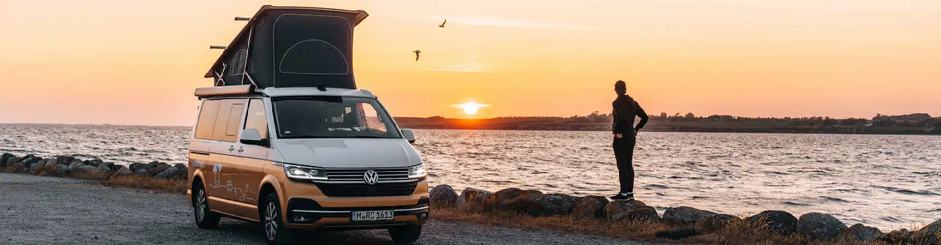 roadsurfer camper van with pop-up roof parked next to a beach at sunset