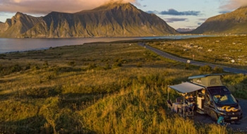 Campervan by the water next to green grass with hill panorama in the background at sunset in Norway