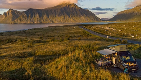 Campervan by the water next to green grass with hill panorama in the background at sunset in Norway