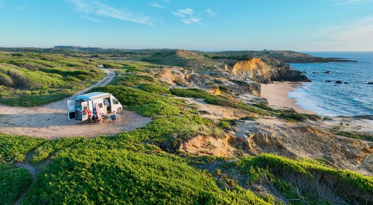 Camper van standing on a hill in Portugal, the coastline below and sand glowing from the setting sun