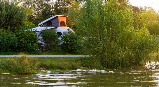 Campervan with open pop up roof standing on a campground in the middle of nature at the lake.