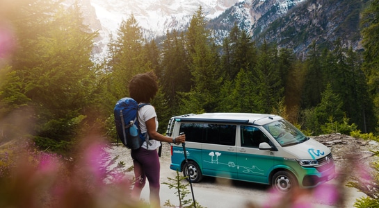 woman starting the hiking route from a turquoise campervan in the mountains of Austria