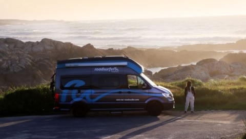 Camper van parked at a coastal overlook with rocky shorelines and ocean waves below
