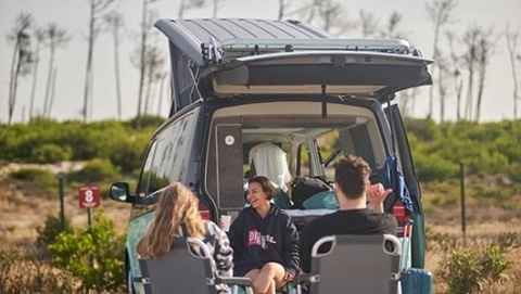 Campers at campsite, sitting outside their camper van in chairs, laughing